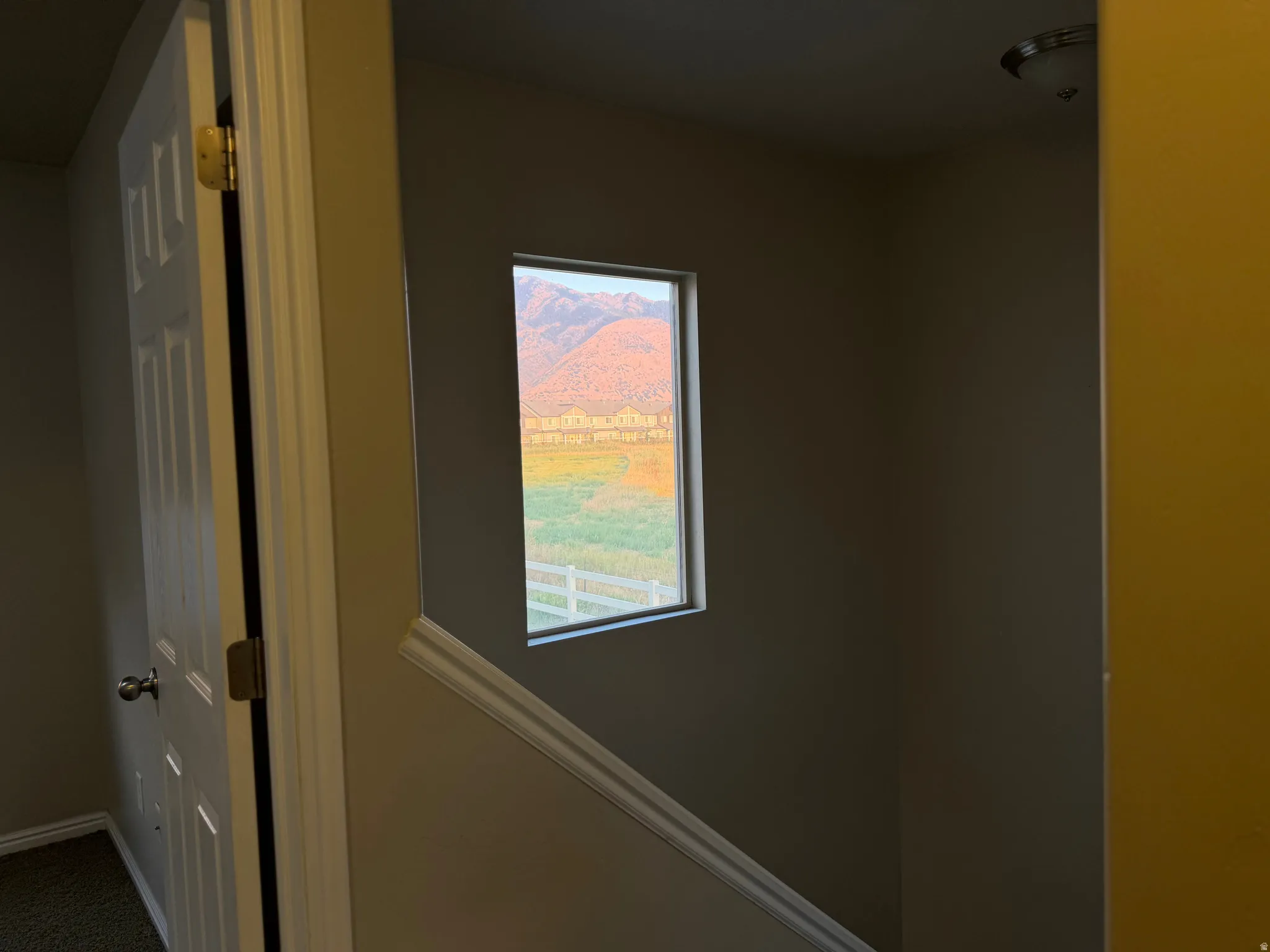 Window featuring a distant mountain range, open field, and white fence