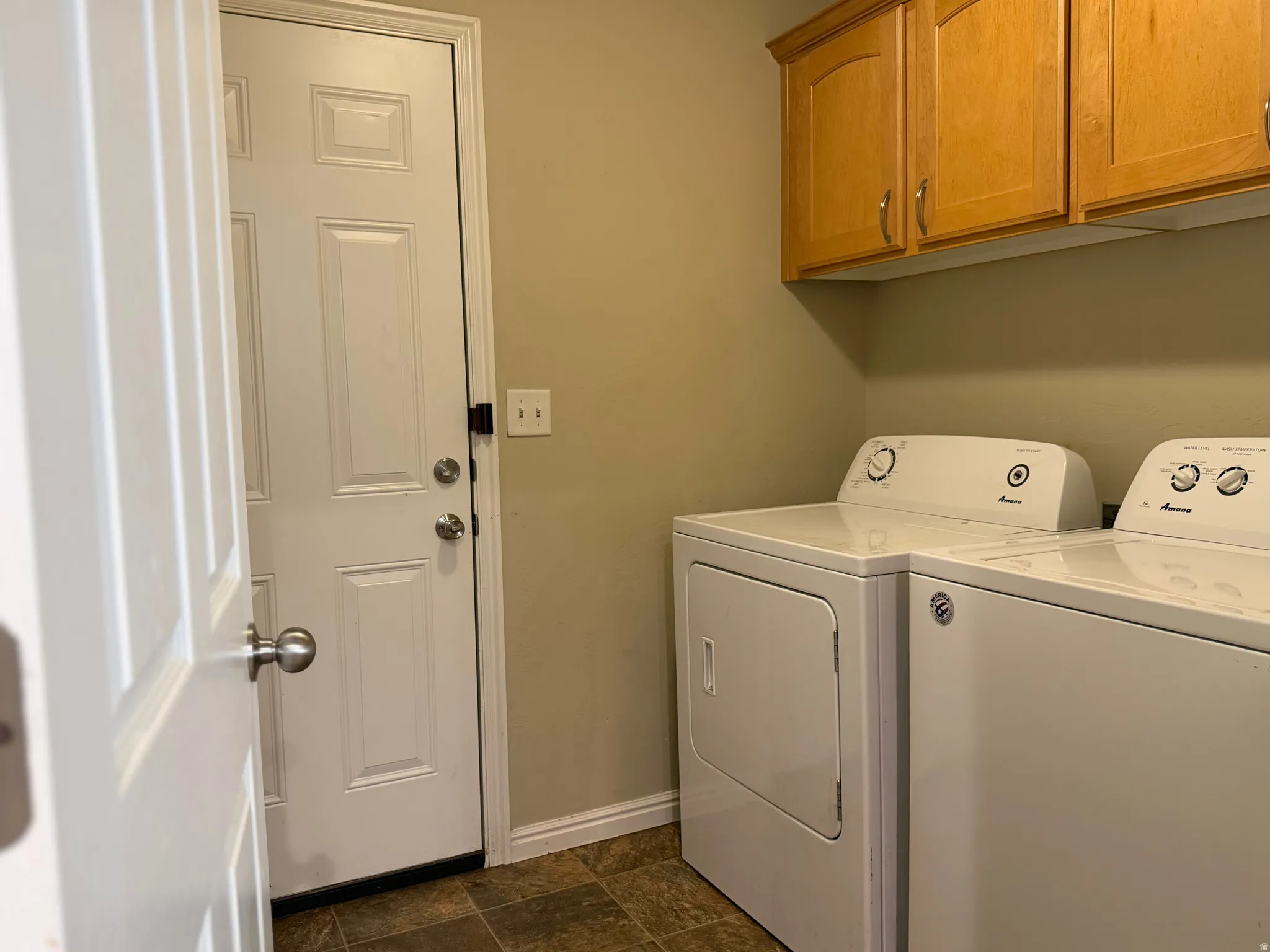 Laundry area featuring wood-finish cabinetry, neutral wall color, and brown tile-pattern flooring