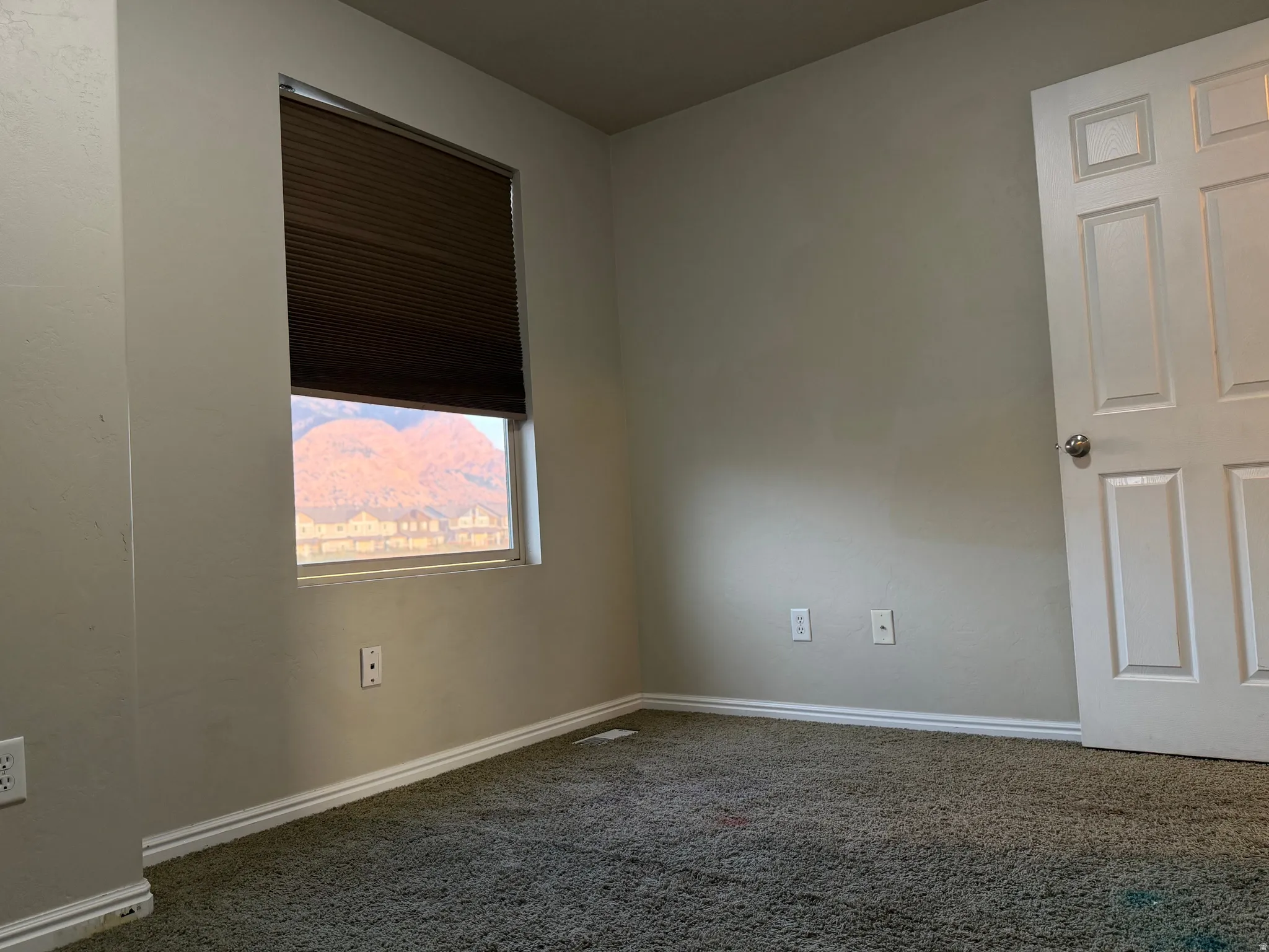 Wall-to-wall carpeted room featuring a window with cellular shades and a panel door