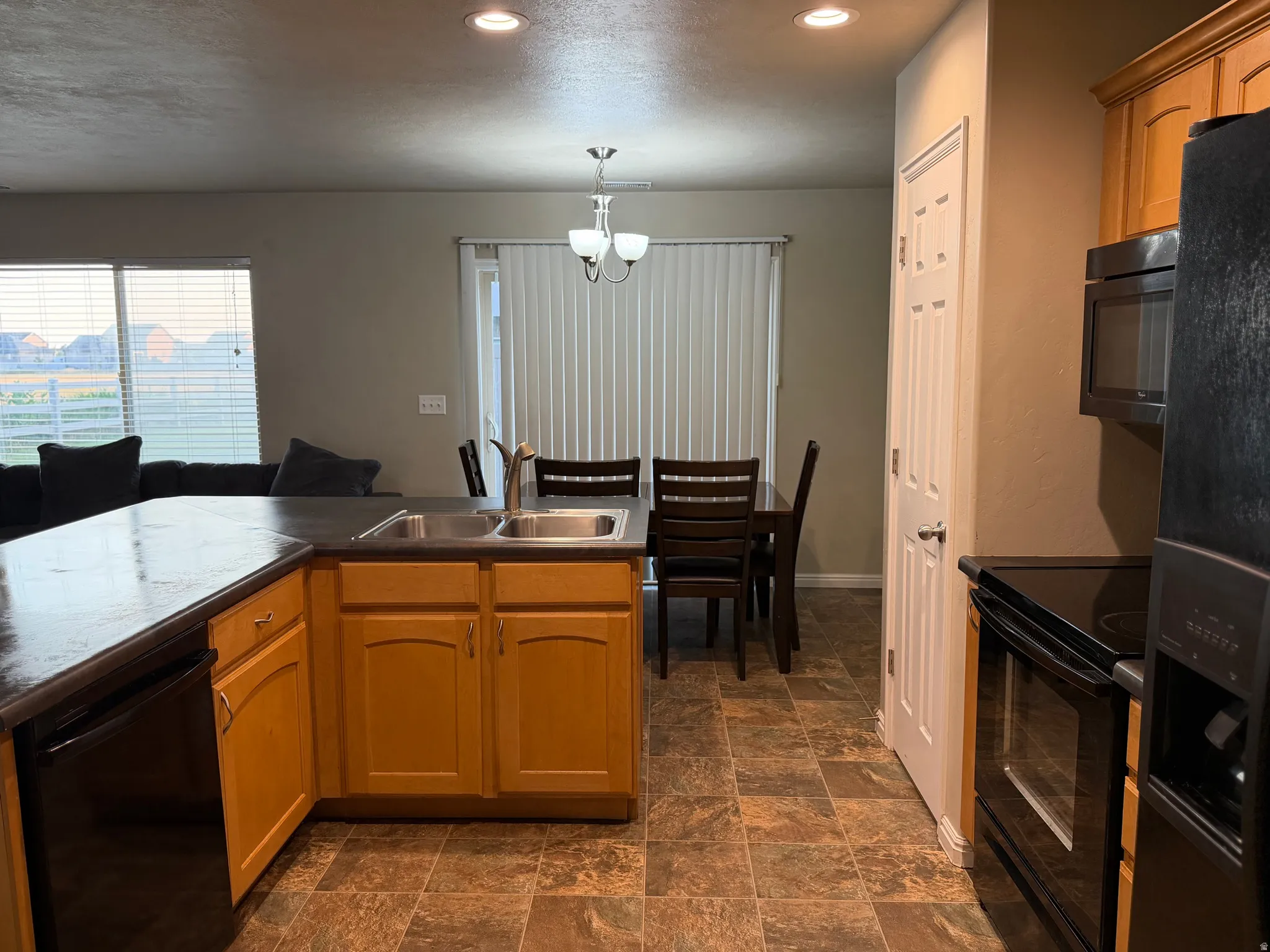 Kitchen featuring wood-finish cabinetry, dark countertops, a double basin sink with a high-arc faucet, and black appliances including a built-in microwave and range