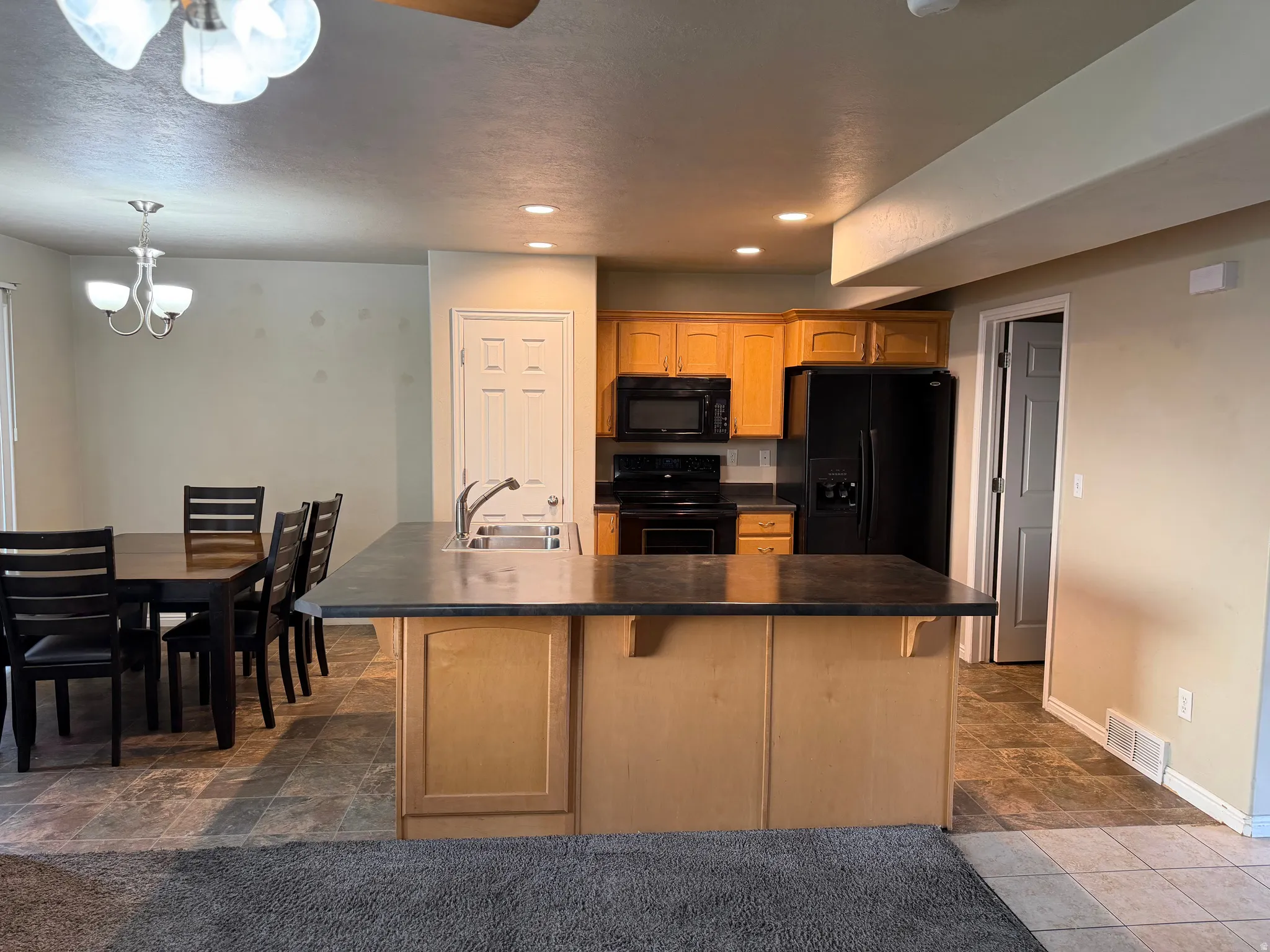 Kitchen island with integrated sink, black appliances, light wood cabinetry, and recessed lighting