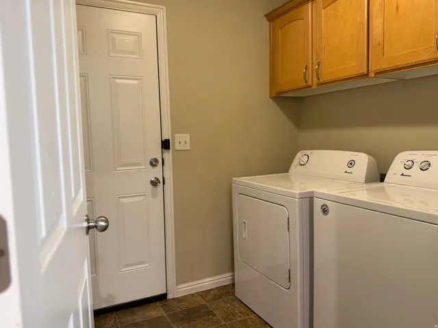 Laundry area featuring wood-finish cabinetry, neutral wall color, and brown tile-pattern flooring