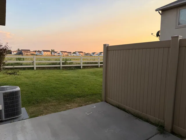 Expansive backyard featuring a green lawn, concrete patio, and a light brown privacy fence
