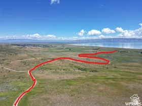 Expansive aerial landscape featuring a large body of water, distant mountains, and a winding dirt road