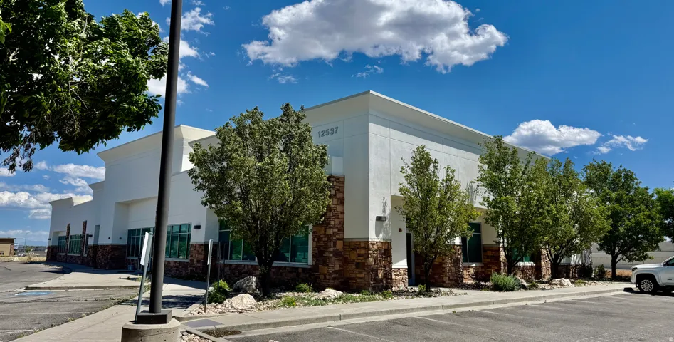 Modern commercial building featuring a stone and stucco exterior, prominent window-line, mature landscaping, and an expansive paved parking area