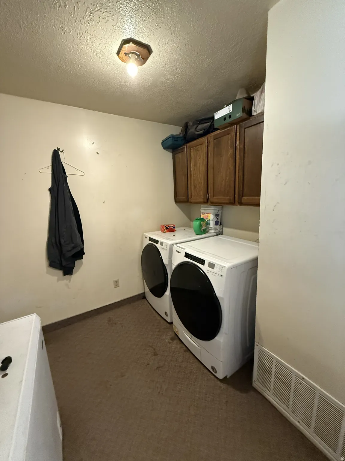 Dedicated laundry area featuring overhead cabinetry, textured ceiling, a flush-mount light fixture, and floor vents