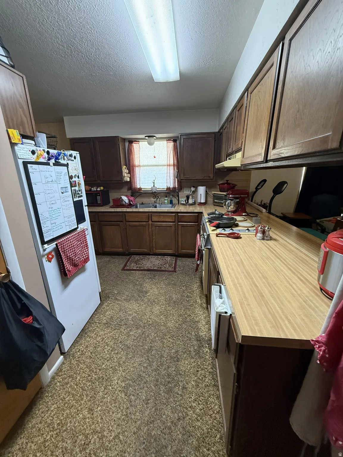 Galley kitchen featuring wood-finish cabinetry, light wood-finish countertops, and a double basin sink beneath a window