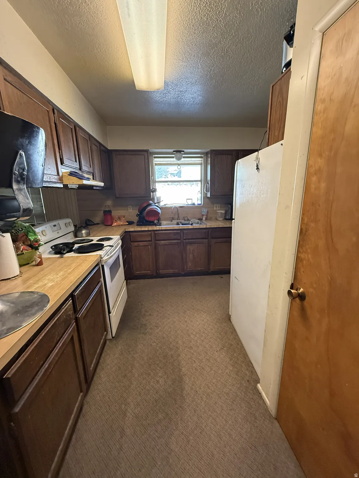 Galley kitchen featuring wood-finish cabinetry, a window over the sink, and a drop-in electric range