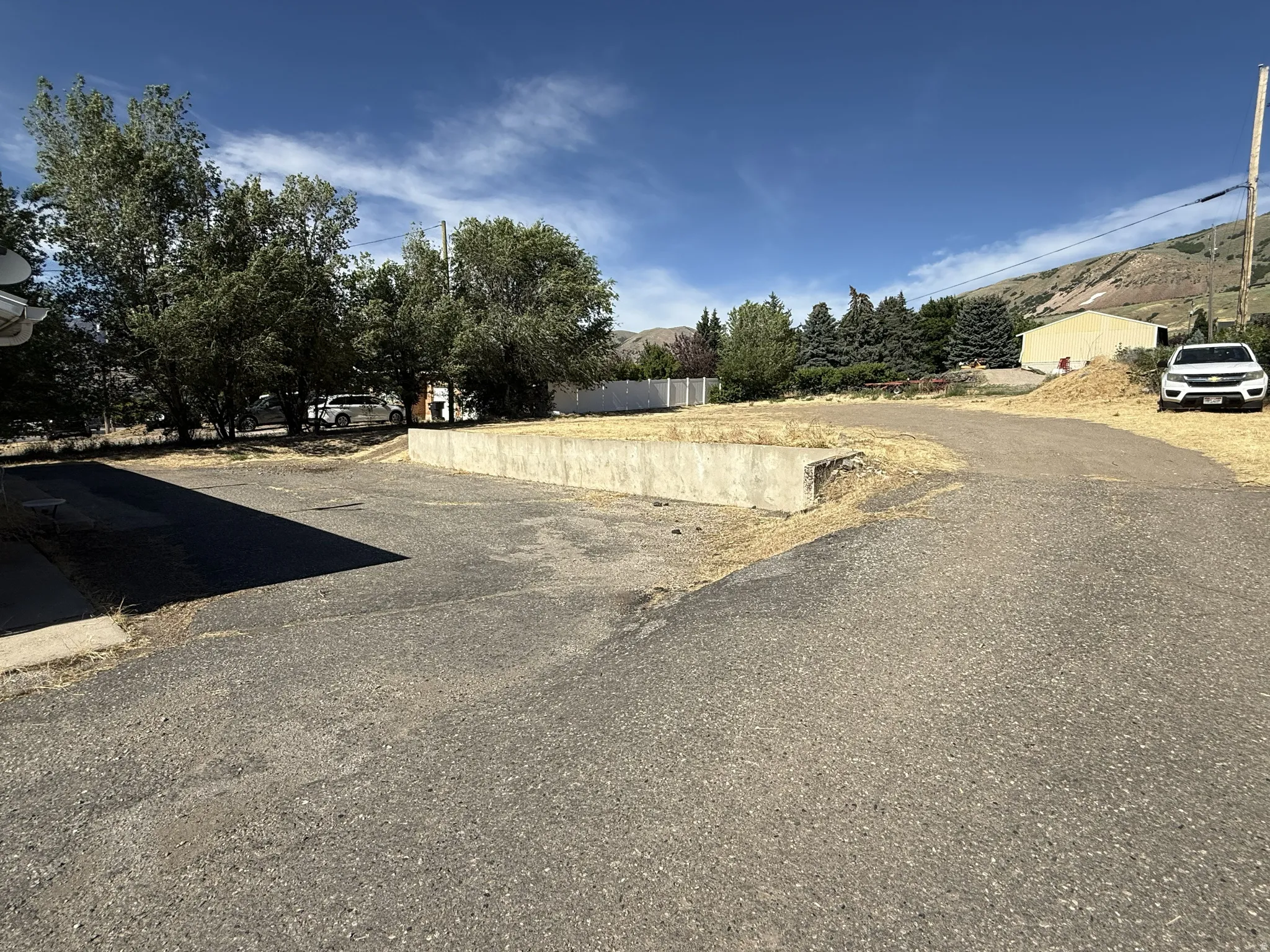 Paved surface and concrete retaining wall with mature trees and mountain backdrop
