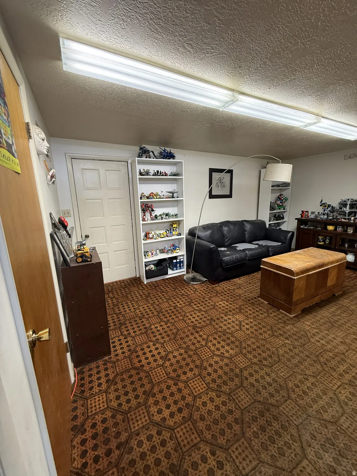 Recessed fluorescent lighting fixtures illuminate a room featuring patterned wall-to-wall carpeting and white painted walls