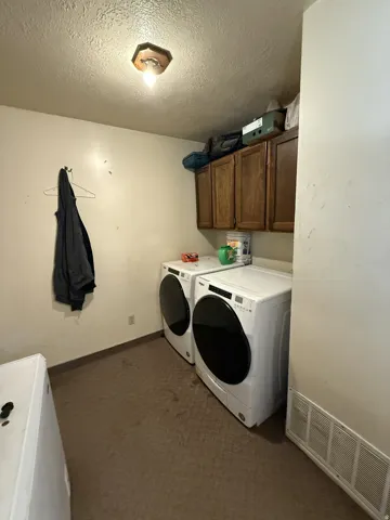 Dedicated laundry area featuring overhead cabinetry, textured ceiling, a flush-mount light fixture, and floor vents