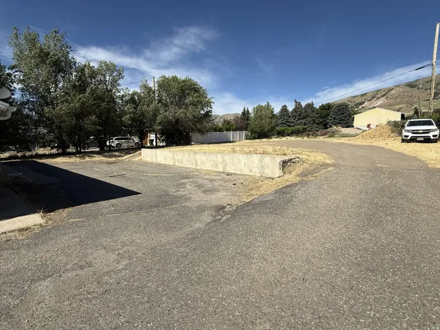 Paved surface and concrete retaining wall with mature trees and mountain backdrop