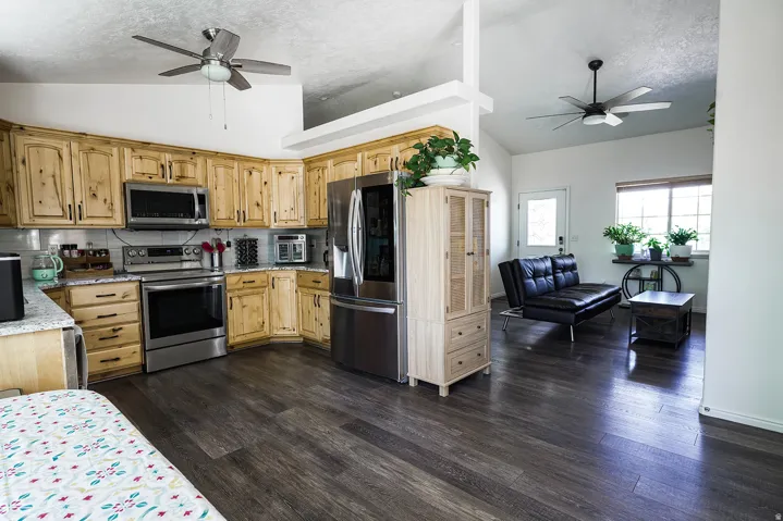 Open-concept kitchen and living area featuring wood-finish flooring, light-toned cabinetry, stainless steel appliances, and a vaulted ceiling with two ceiling fans