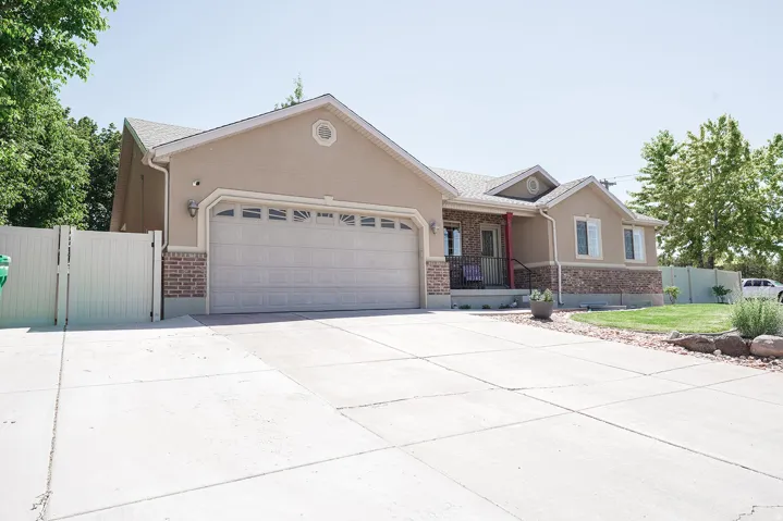 Stucco and brick exterior with a large two-car garage, concrete driveway, and a covered front porch with dark railings