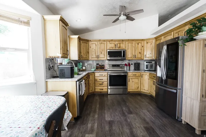 Kitchen featuring wood-finish flooring, light wood cabinetry, stainless steel appliances, and a tile backsplash