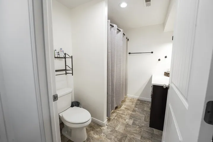 Compact bathroom featuring wood-finish flooring, a white toilet, and a dark wood-finish vanity with a white countertop