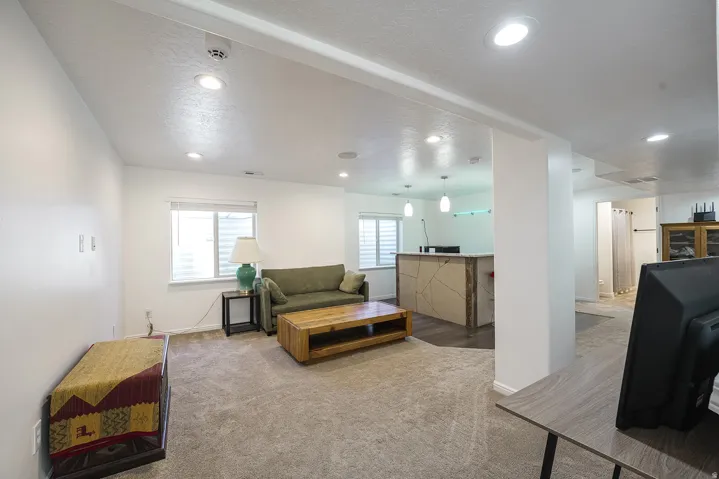 Carpeted living area featuring recessed lighting, a window with horizontal blinds, and a built-in bar with pendant lighting and a decorative front panel
