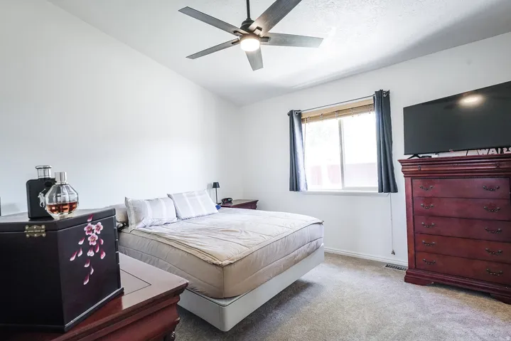 Interior room featuring light-colored carpeting, a window with dark curtain panels, a ceiling fan with integrated lighting, and white wall finishes