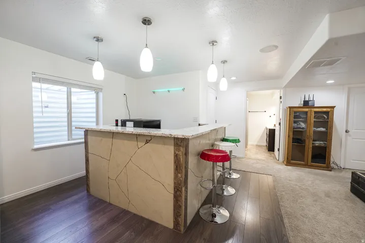 Entertainment space featuring a stone-finish bar with a light-toned countertop, wood-finish flooring, and recessed lighting
