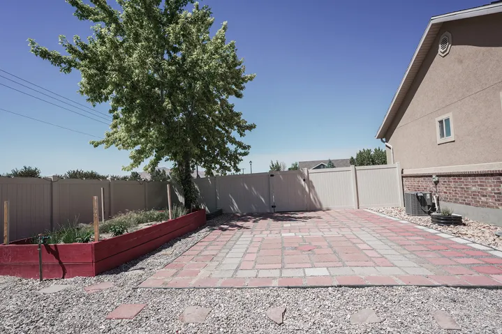 Expansive outdoor space featuring a decorative paver patio, a raised garden bed, and a mature shade tree