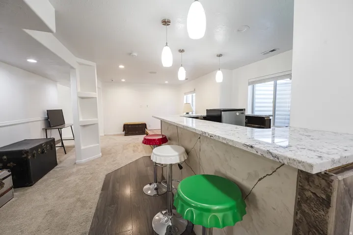 Spacious recreational room featuring a stone-look bar with a light-toned countertop, pendant lighting, recessed lighting, and carpet flooring
