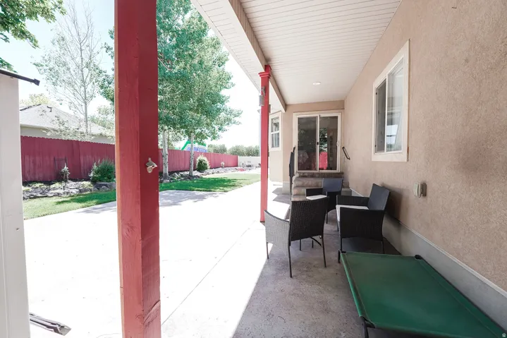 Covered patio featuring a concrete surface, red-stained support pillars, stucco exterior, and white framed windows