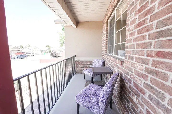 Covered front porch featuring a multi-tone brick facade, stucco siding, a white-framed window, and black metal railing