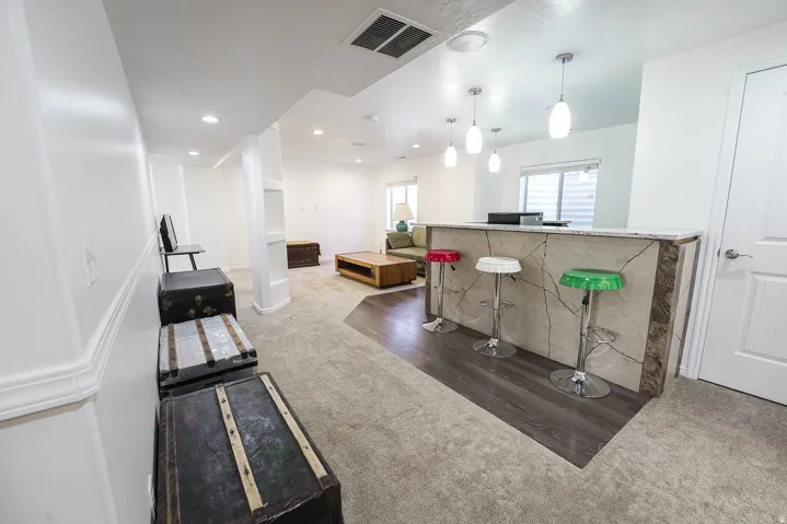 Spacious room featuring a bar with a stone-finish countertop, pendant lighting, built-in shelving, carpet flooring, and recessed lighting
