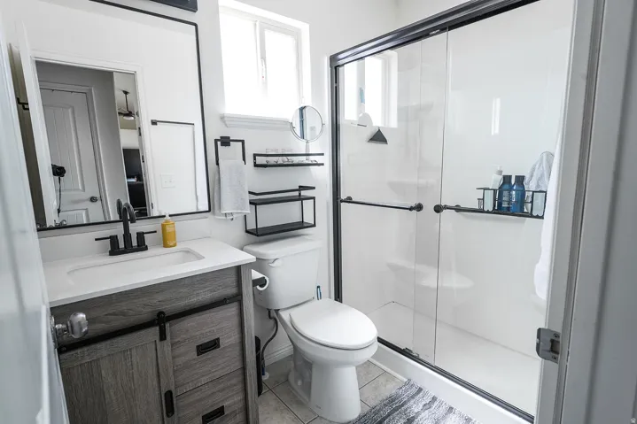 Bathroom featuring a grey wood-finish vanity with a white countertop and rectangular sink, matte black faucet, and a frameless mirror