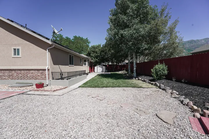 Expansive backyard featuring a gravel patio, manicured lawn, and mature trees