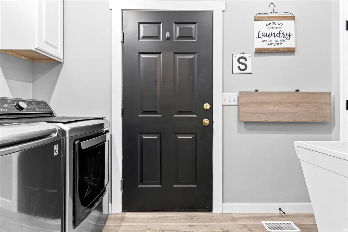 Dedicated laundry space featuring a paneled door, light gray walls, white baseboards, and wood-finish flooring