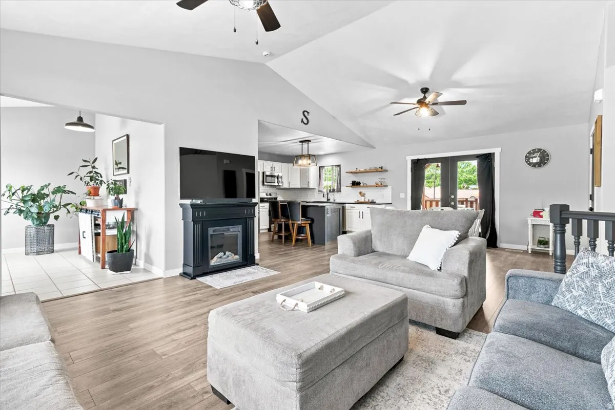 Vaulted ceilings enhance this open-concept living area featuring wood-finish flooring, a contemporary fireplace, and ceiling fans