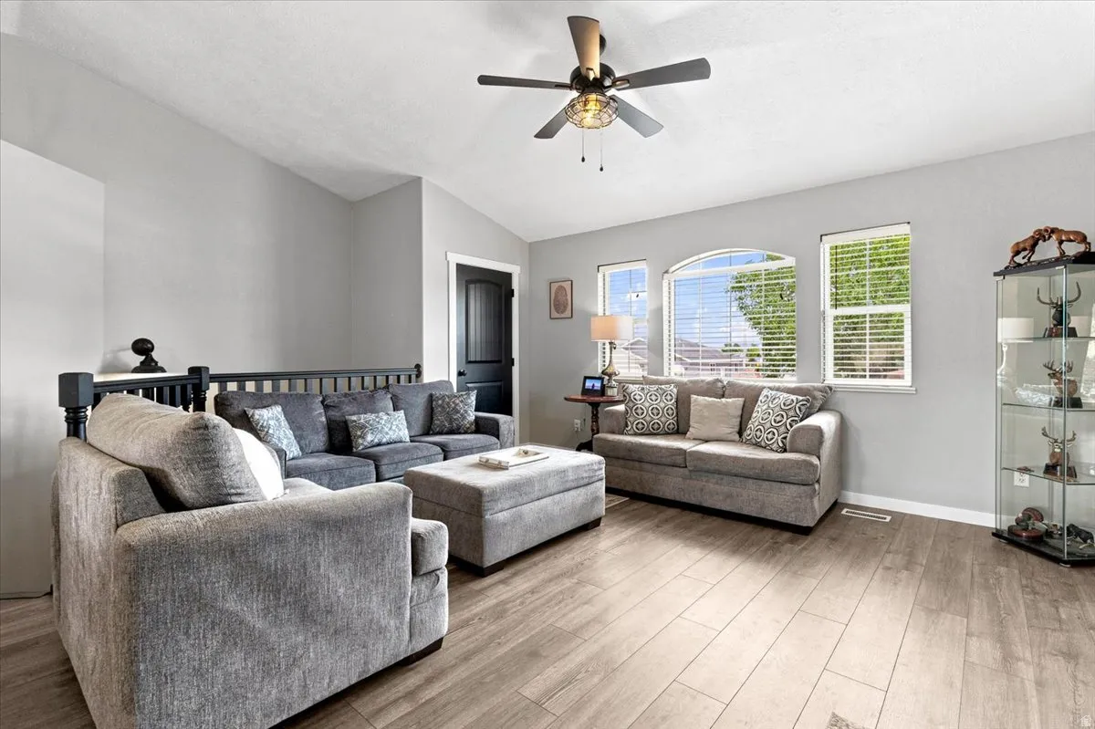 Spacious living area featuring vaulted ceilings, wood-finish flooring, a ceiling fan with integrated lighting, and multiple windows including an arched window