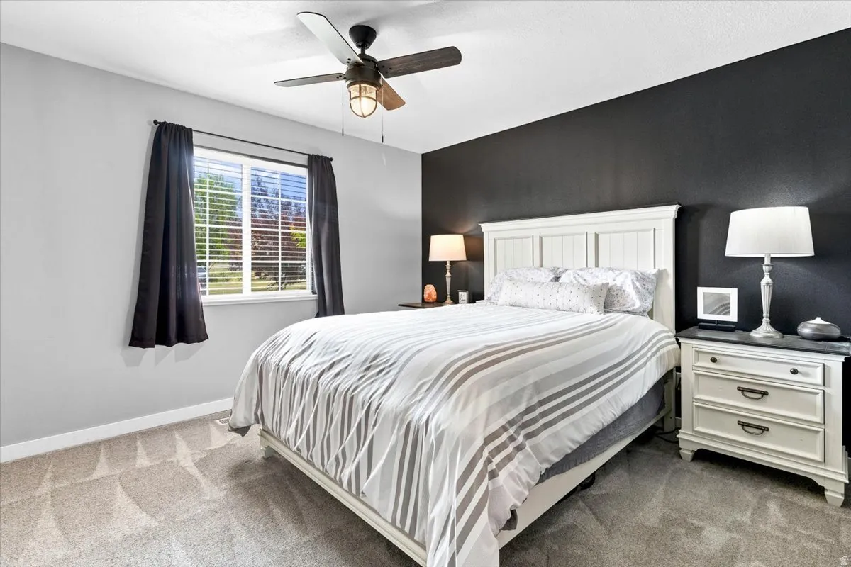 Master bedroom featuring a ceiling fan, a window with blinds, and new carpet flooring