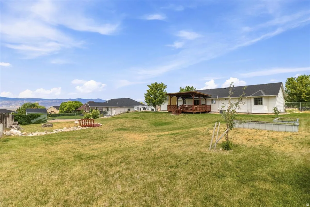 Expansive backyard featuring a covered wood deck, mature trees, a garden bed, and a decorative bridge over a dry creek bed