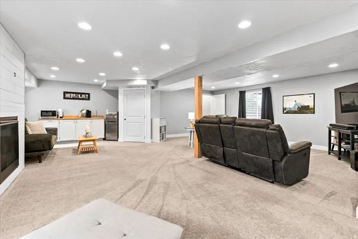 Spacious lower-level area featuring recessed lighting, light-toned carpeting, a built-in wet bar with white cabinetry and wood-finish countertops, and a paneled accent wall