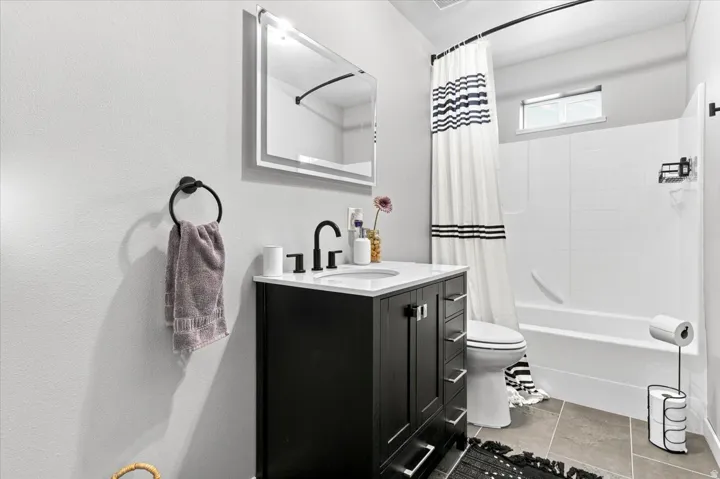 Main level bathroom featuring a dark wood-finish vanity with a white countertop and rectangular sink, matte black faucet, and a LED touchscreen mirror.