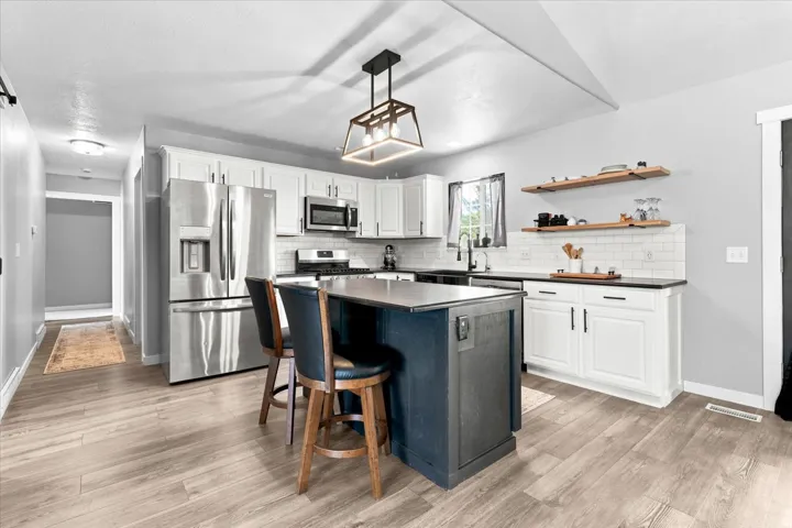 Modern kitchen featuring an island with seating, stainless steel appliances, wood-finish flooring, white cabinetry, and a subway tile backsplash