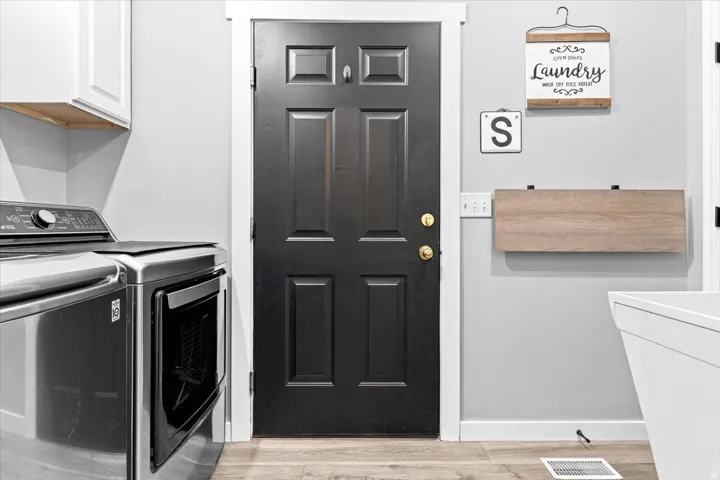 Dedicated laundry space featuring a paneled door, light gray walls, white baseboards, and wood-finish flooring