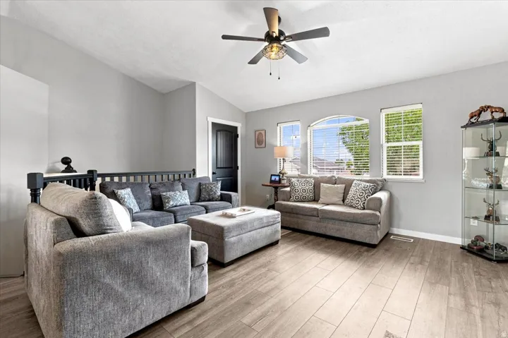 Spacious living area featuring vaulted ceilings, wood-finish flooring, a ceiling fan with integrated lighting, and multiple windows including an arched window