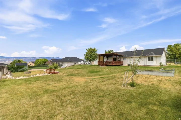 Expansive backyard featuring a covered wood deck, mature trees, a garden bed, and a decorative bridge over a dry creek bed