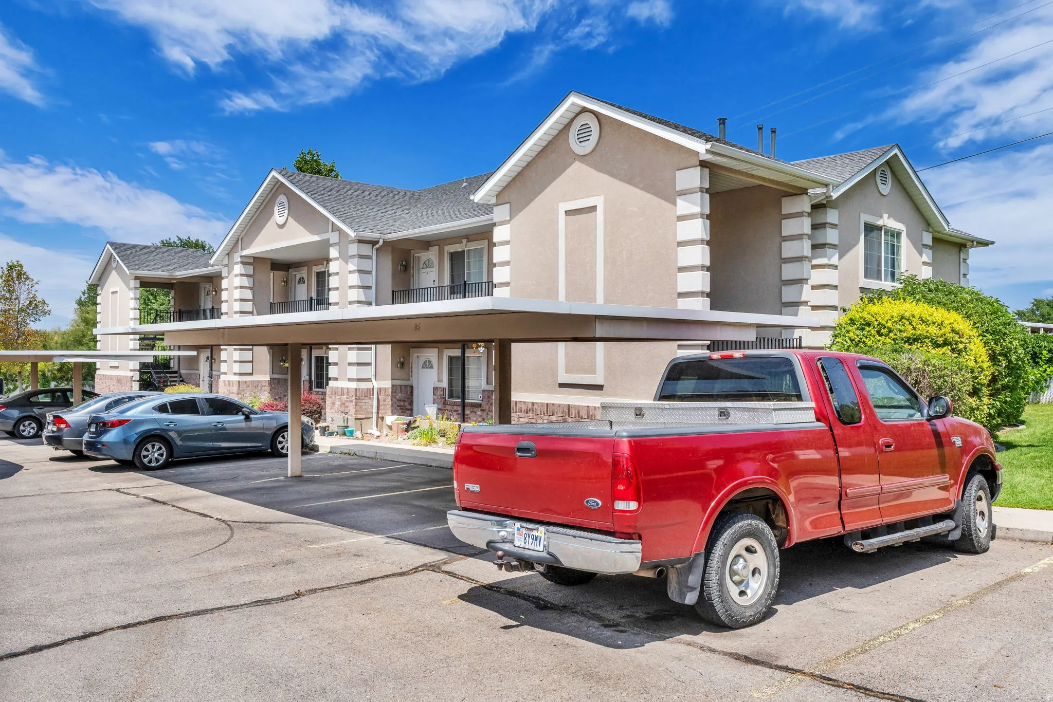 Multi-unit residential buildings featuring stucco and brick veneer exteriors, gabled roofs, and covered parking structures