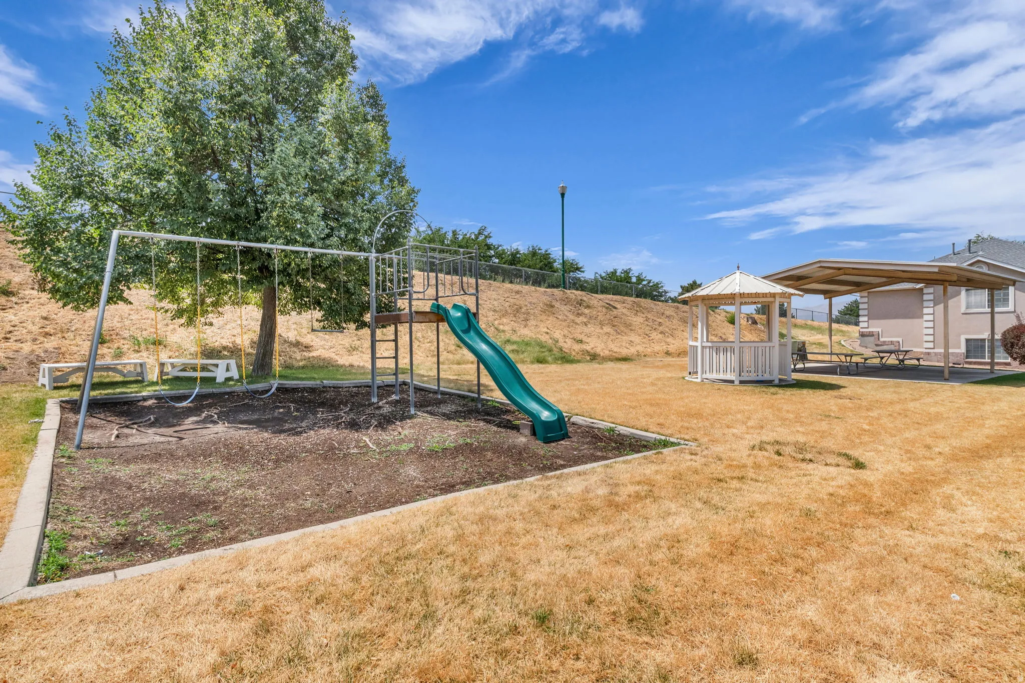 Outdoor recreational area featuring a swing set, slide, shaded gazebo, and covered patio with picnic tables