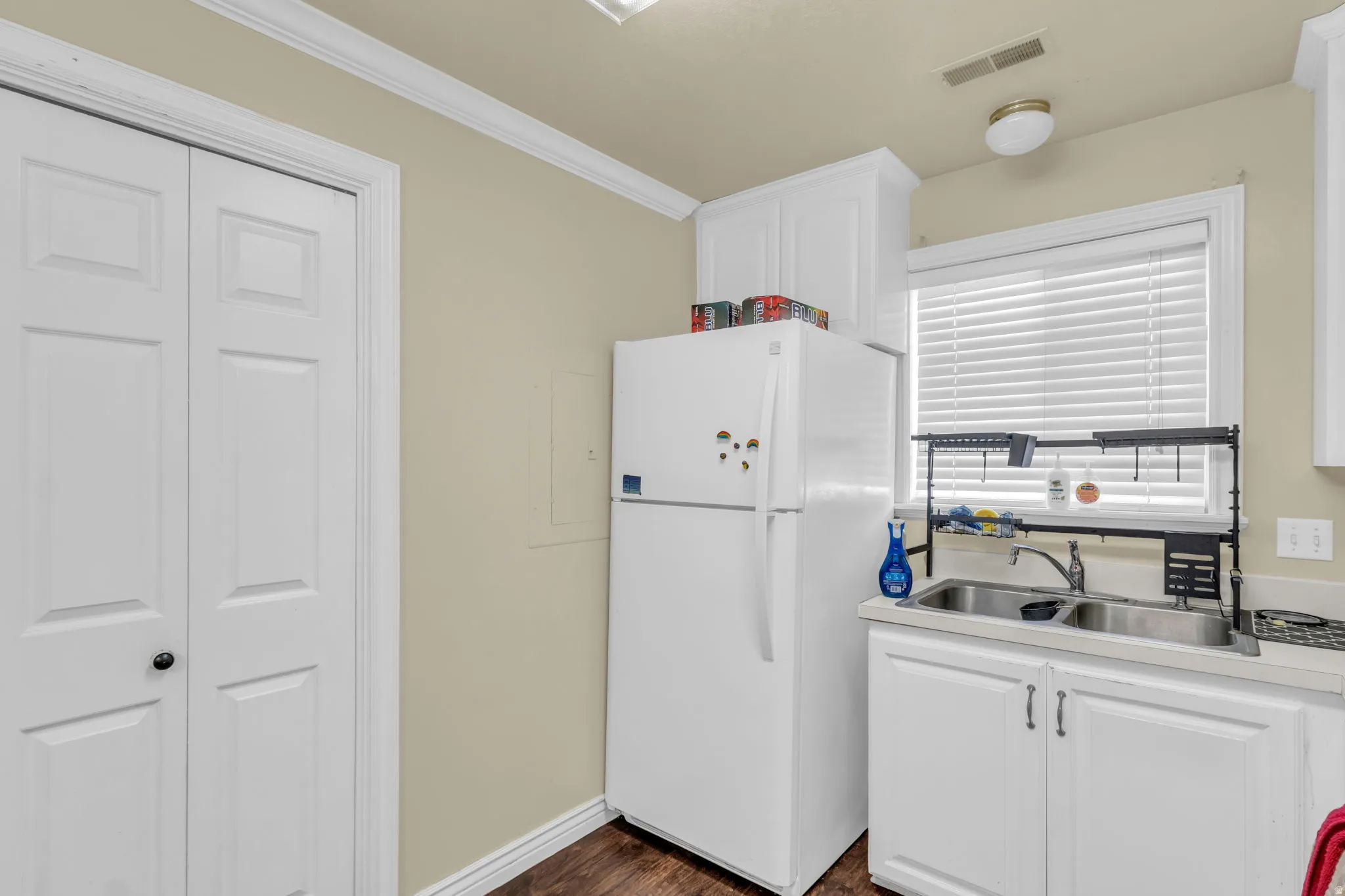 Kitchen area with white cabinetry, a double basin stainless steel sink, and a window with blinds