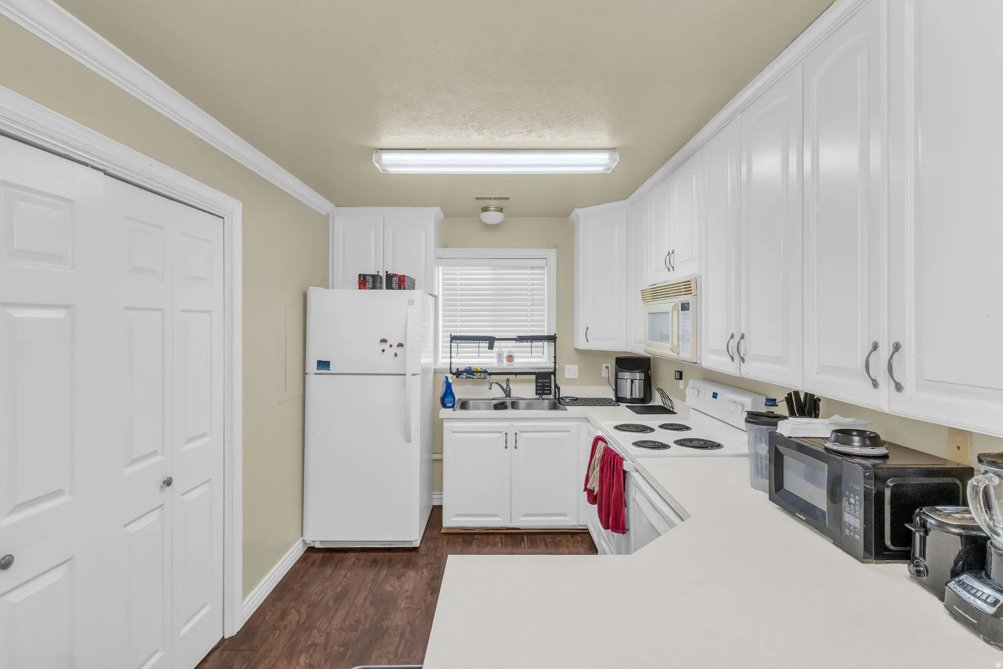 Kitchen with white cabinetry, wood-finish flooring, light countertops, and built-in microwave