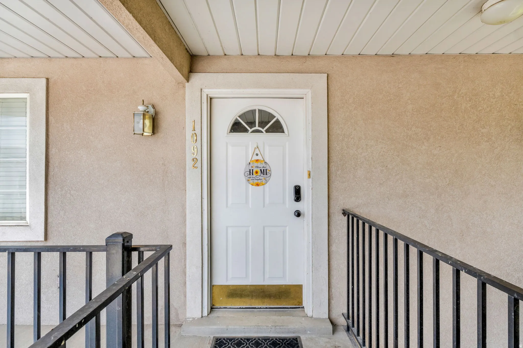 Front entry featuring a paneled door with an arched window, stucco siding, and a covered porch with a slatted ceiling