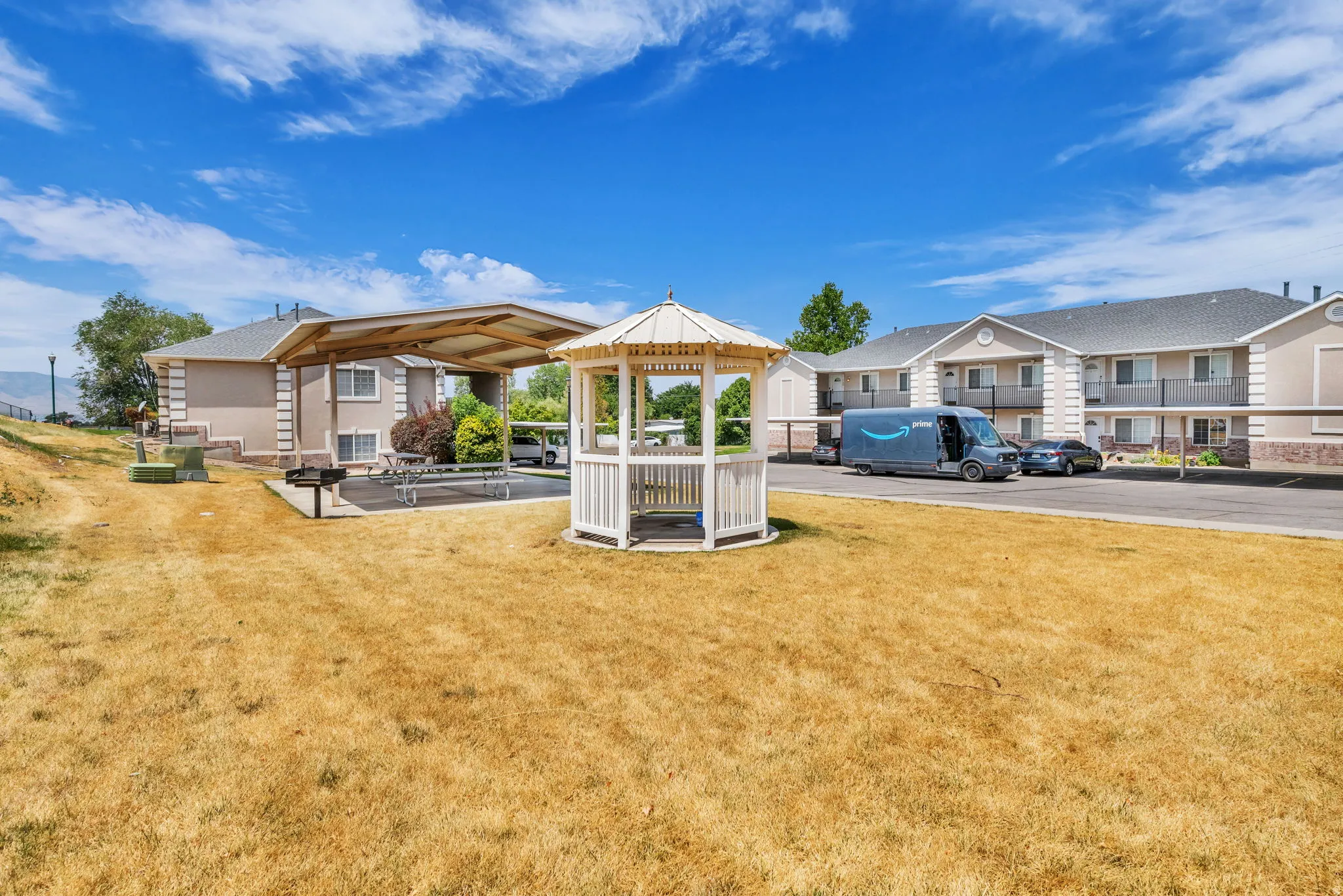 Community grounds featuring a white gazebo, shaded picnic area with seating, and a built-in barbecue grill