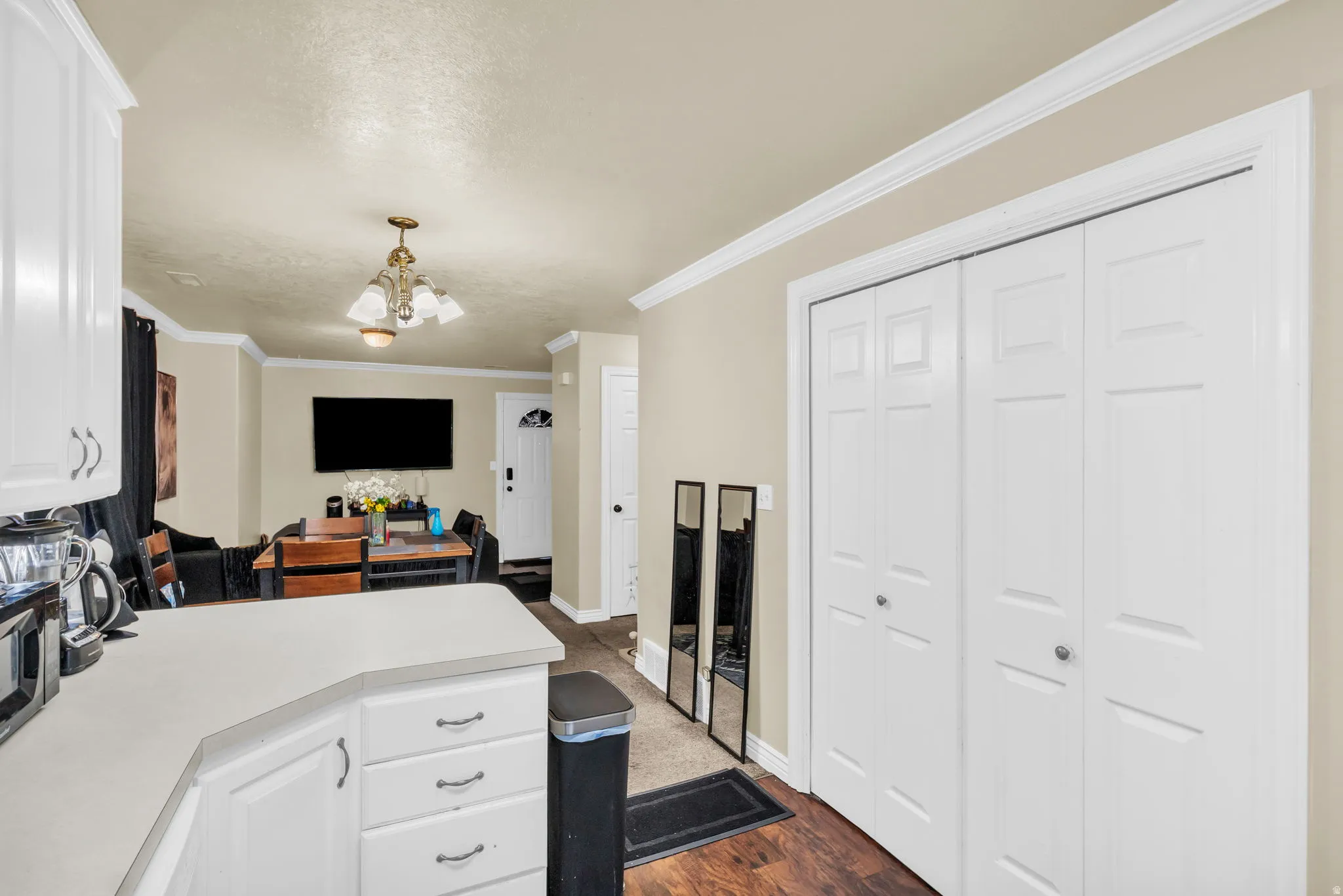 White shaker-style cabinetry with chrome hardware, light-toned countertop, wood-finish flooring, and crown molding