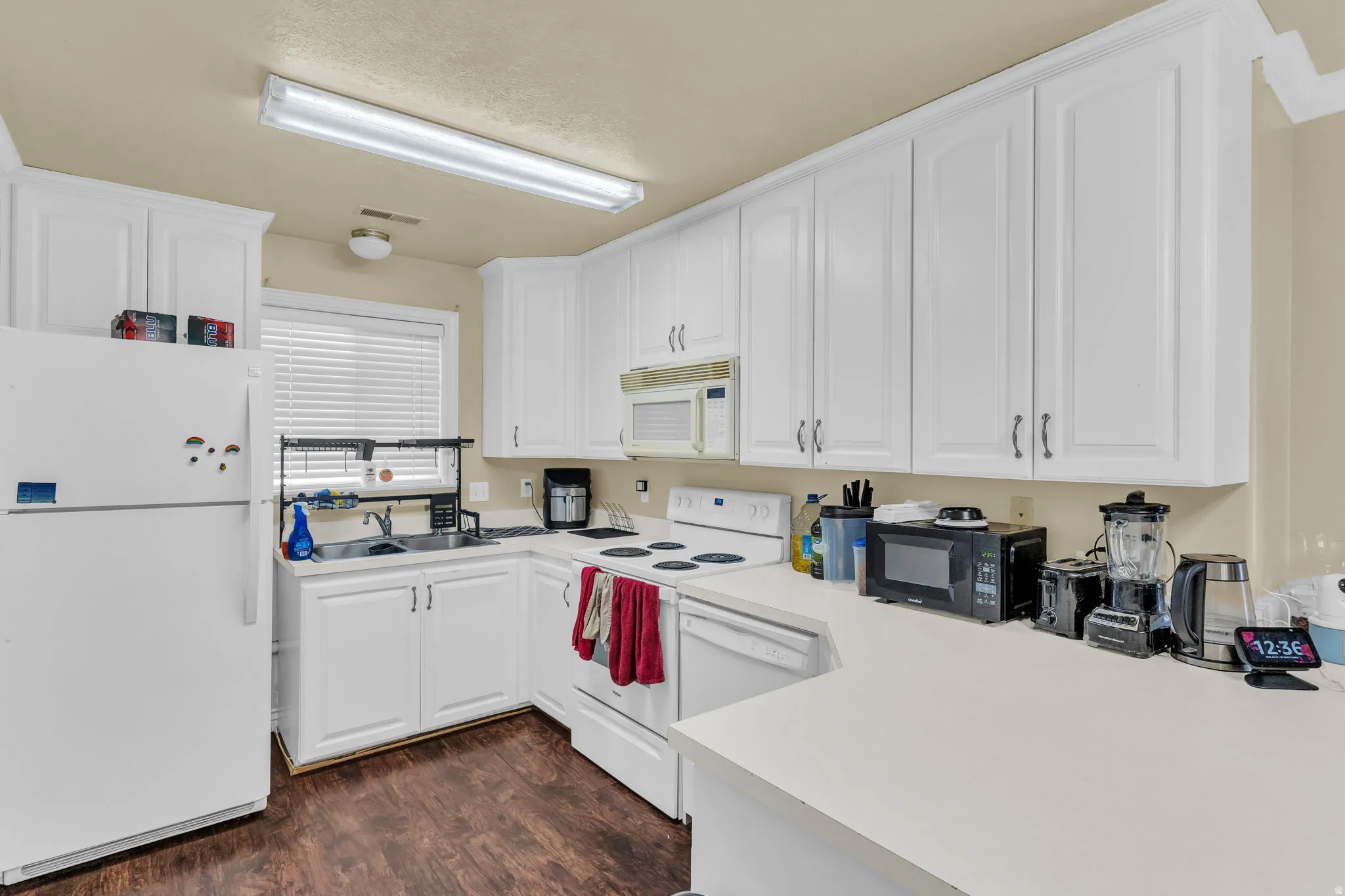Kitchen featuring abundant white cabinetry, light-toned countertops, and wood-finish flooring