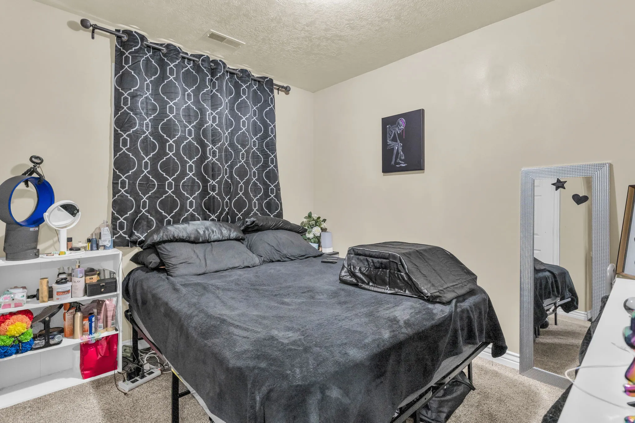 Carpeted room with a textured ceiling and a window featuring patterned curtains